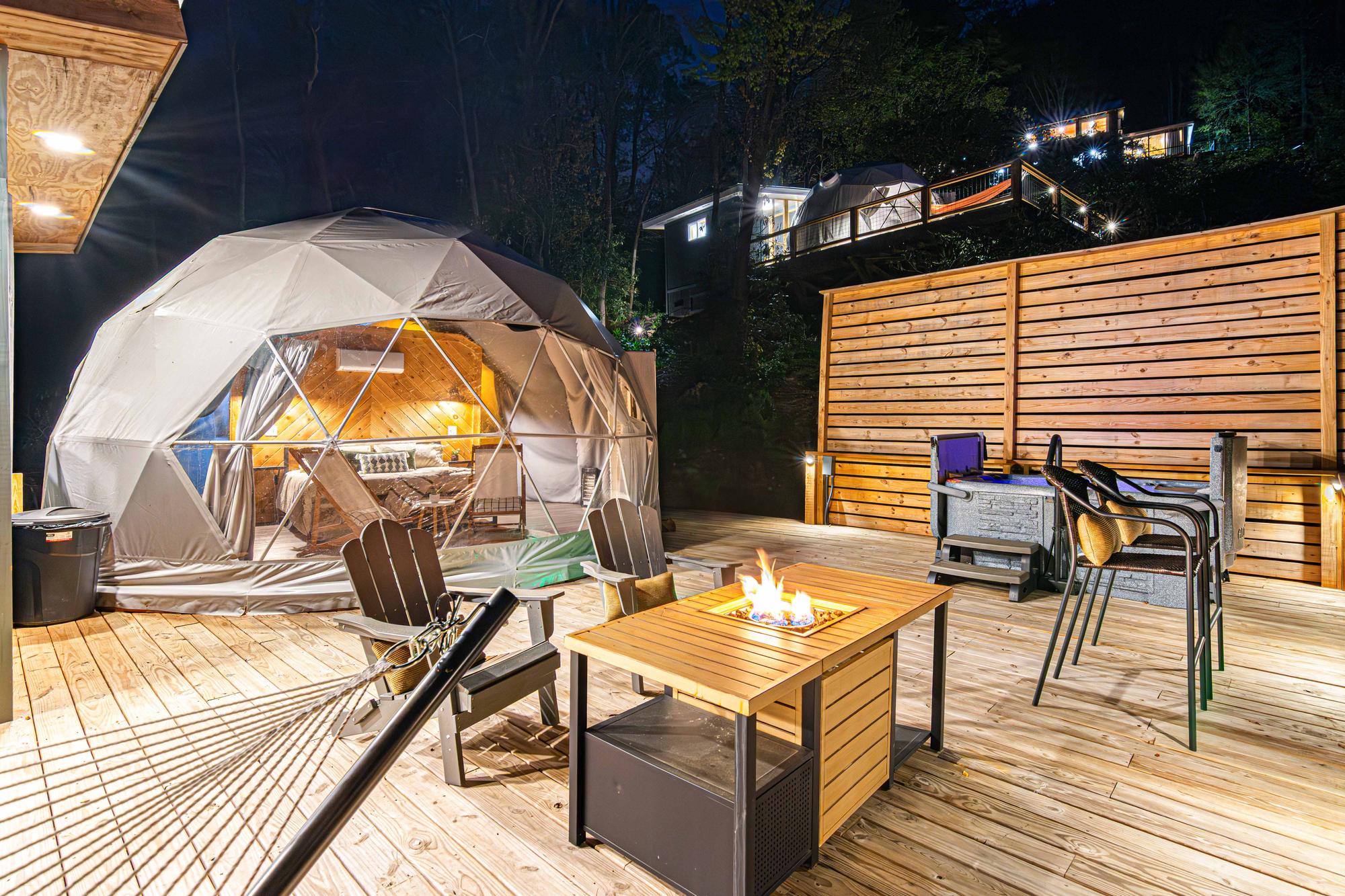 Both geodesic domes at dusk — the lower dome on its deck in the foreground, the upper dome lit on the hillside above