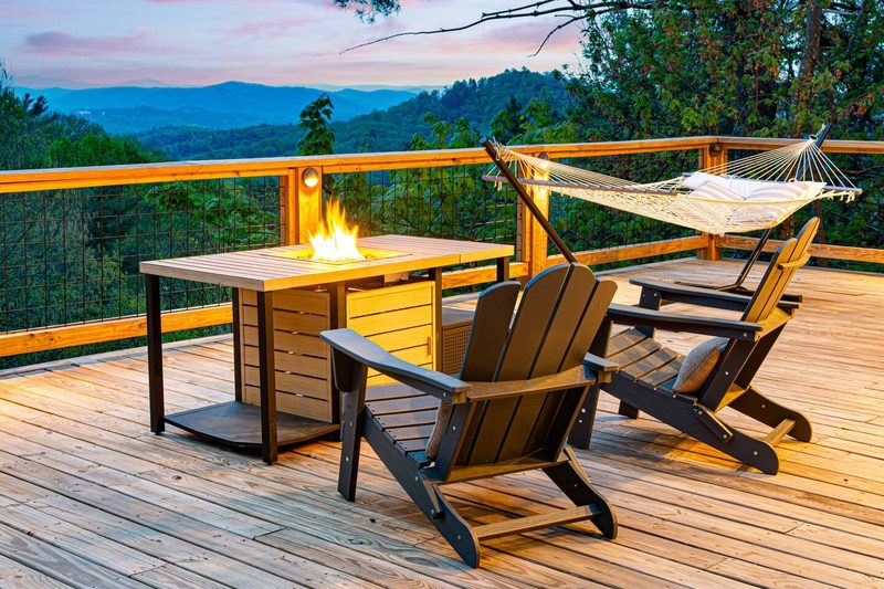 A wooden deck in Blowing Rock, NC, with Adirondack chairs around a fire pit table, a hammock on the right, and a stunnin