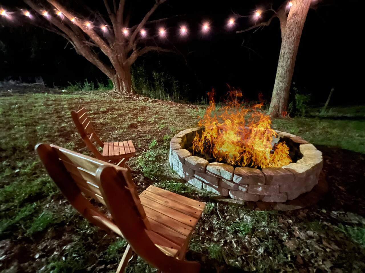 Fire pit ringed with string lights in the fenced yard