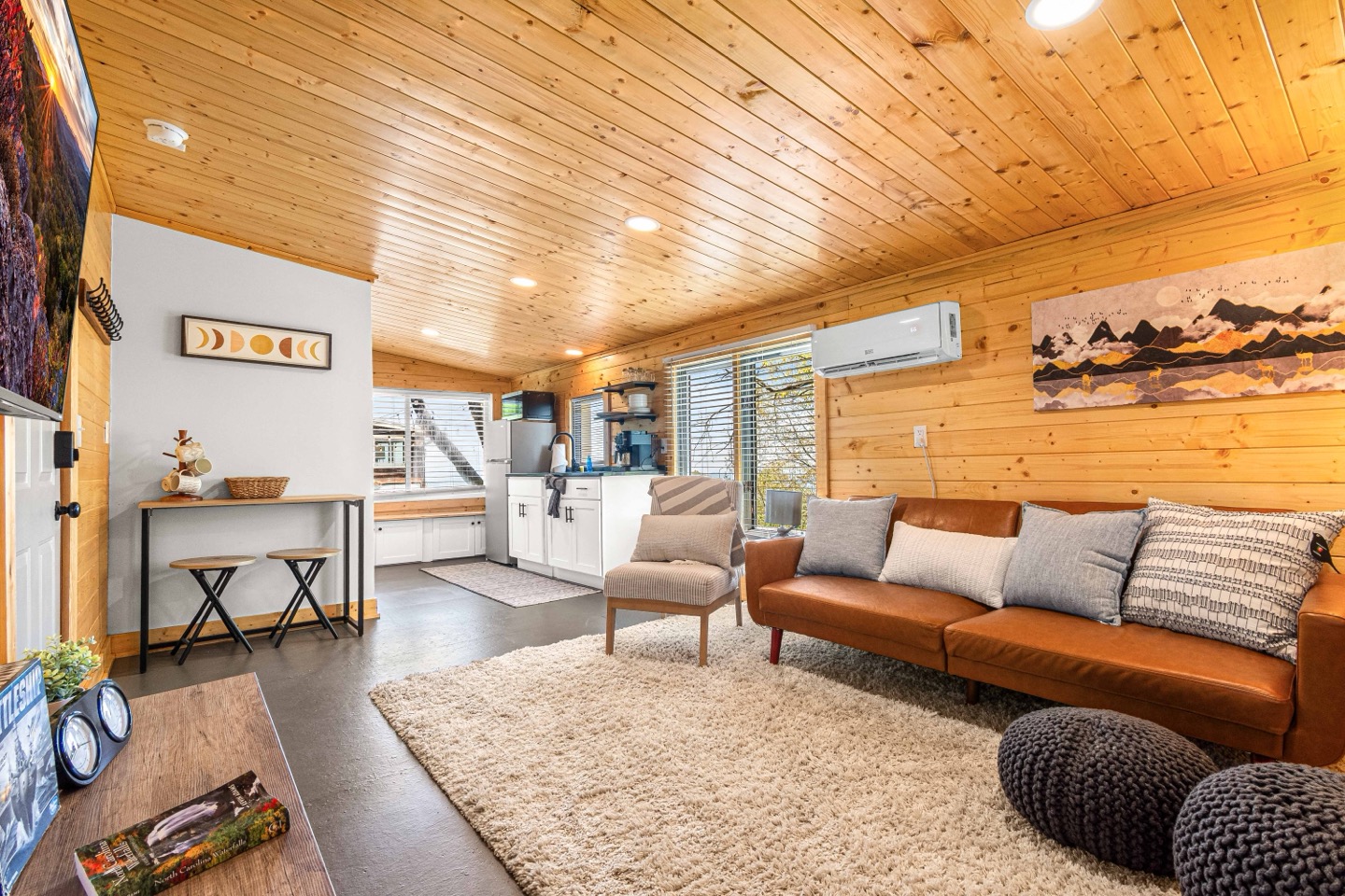 Living area with a leather sofa under spruce tongue and groove, kitchenette beyond